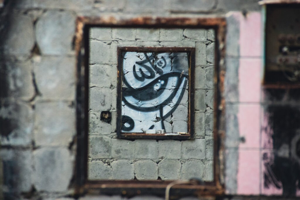 Eine Nahaufnahme eines mit Graffiti dekorierten Rahmens, der durch eine Reihe von Fenstermauern aus grauen Betonblöcken schaut.
